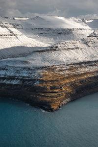 Majestic scenery of rocky terrain covered with snow near calm sea on cloudy day on faroe islands