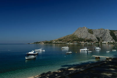 Boats moored in sea against clear blue sky