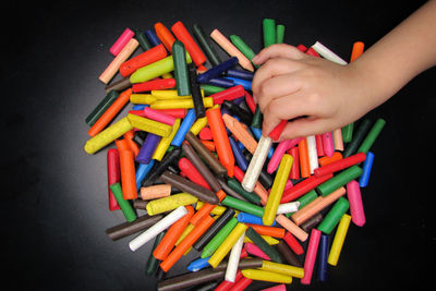 High angle view of hand holding multi colored pencils against black background