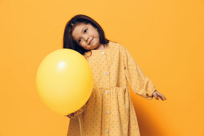 Portrait of young woman with balloons against yellow background