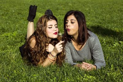 Mother and daughter blowing dandelion while lying on grass