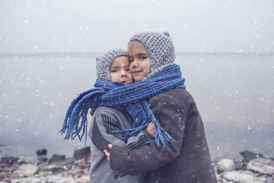 Portrait of smiling siblings embracing by lake during winter