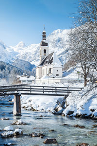 Snow covered church by river against sky