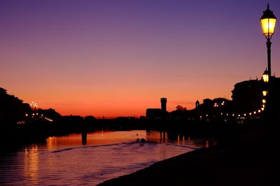 Illuminated street light by silhouette city against orange sky