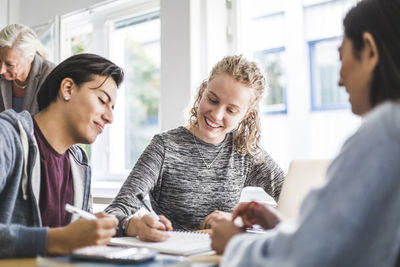 Smiling young woman discussing with male friend over book in classroom