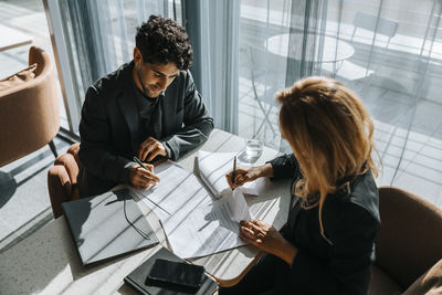 High angle view of businesswoman doing paperwork with male client while at desk in office