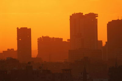 Silhouette buildings against orange sky during sunset