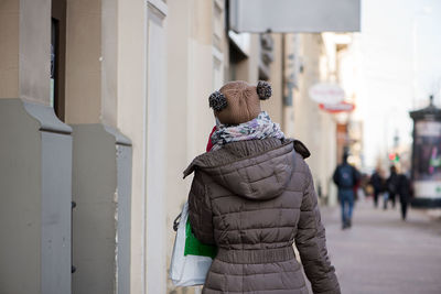 Rear view of woman wearing jacket on sidewalk in city