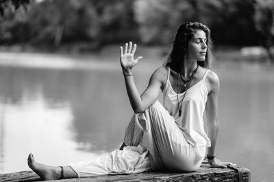 Full length of woman doing yoga while sitting on pier at lake