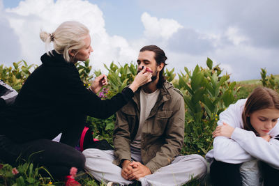 Woman applying make-up on man while sitting outdoors