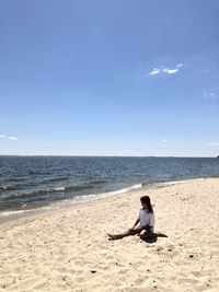 Woman sitting on beach against sky