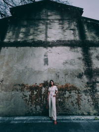 Full length portrait of woman standing against building