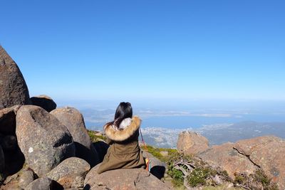 People sitting on rock by sea against clear blue sky