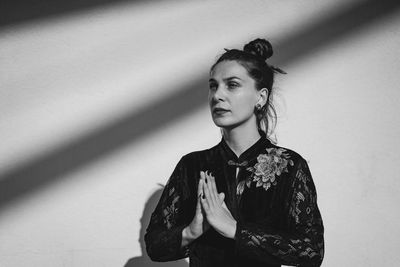 Young woman standing against wall meditating