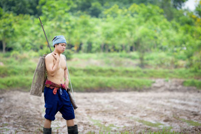 Full length of shirtless man standing against trees