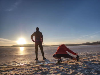 Woman and man stretching in winter nature before run. two sports people working out on frozen lake