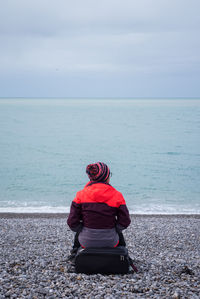 Rear view of woman sitting on beach looking at sea