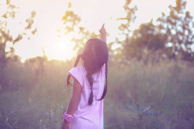 Rear view of woman standing on field against sky during sunset