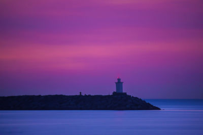 Lighthouse by sea against sky at sunset