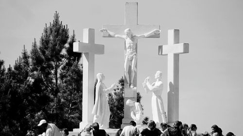 People visiting religious statues outside sanctuary of fatima against clear sky