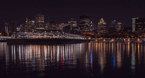 Illuminated buildings by river against sky at night