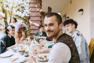 Portrait of smiling gay man sitting with lgbtq friends during dinner party in back yard