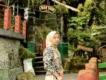 Portrait of young woman standing against trees