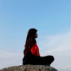 Side view of smiling woman sitting on rock formation against sky