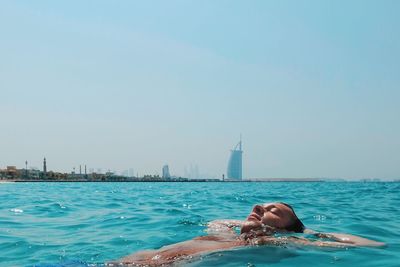 Shirtless man swimming in sea with burj al arab against clear blue sky