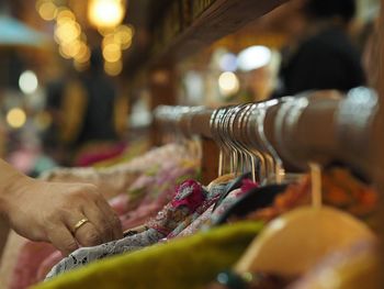 Cropped hand choosing clothes hanging on rack in store