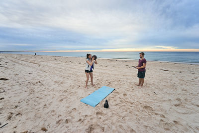 Friends exercising with ball at beach against sky