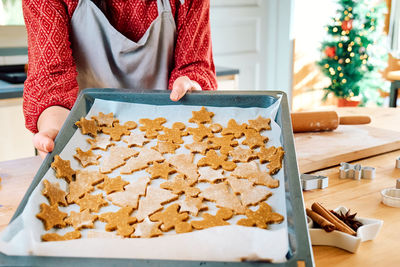 Woman holding baking sheet with christmas gingerbread cookies.