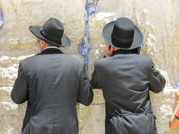 Rear view of men in hats standing against wall