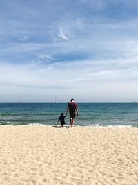 Full length of man with daughter walking on shore at beach against sky