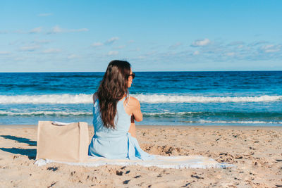 Rear view of woman standing at beach against sky