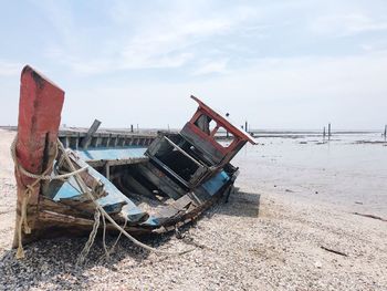 Abandoned boat moored at beach against sky