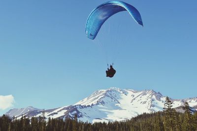 Low angle view of silhouette person paragliding over landscape against blue sky