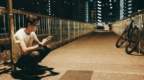 Man sitting below street light looking at mobile phone on bridge