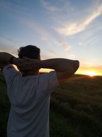 Rear view of man standing on field against sky during sunset