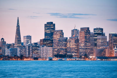 Illuminated buildings by sea in city against sky