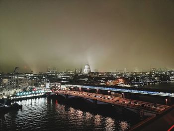 Illuminated bridge over river against buildings in city