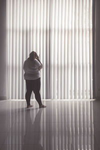 Rear view of overweight woman standing against window at home