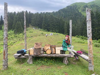 Woman sitting on stone wall by trees in forest