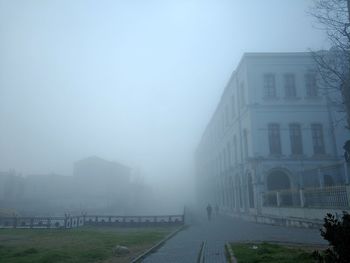 Footpath by buildings against sky during foggy weather