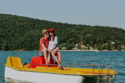 Cheerful man and woman in paddleboat on lake against sky