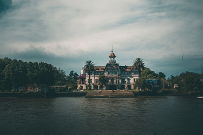 View of buildings by river against cloudy sky