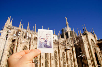 Cropped hand of man holding photograph against milan cathedral