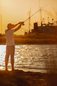 Rear view of woman standing in sea against sky during sunset