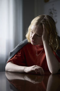 Pensive teenage girl sitting at table with head in hands