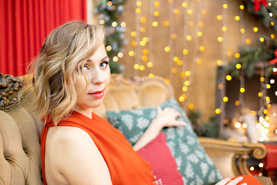 Portrait of young woman standing against illuminated christmas tree